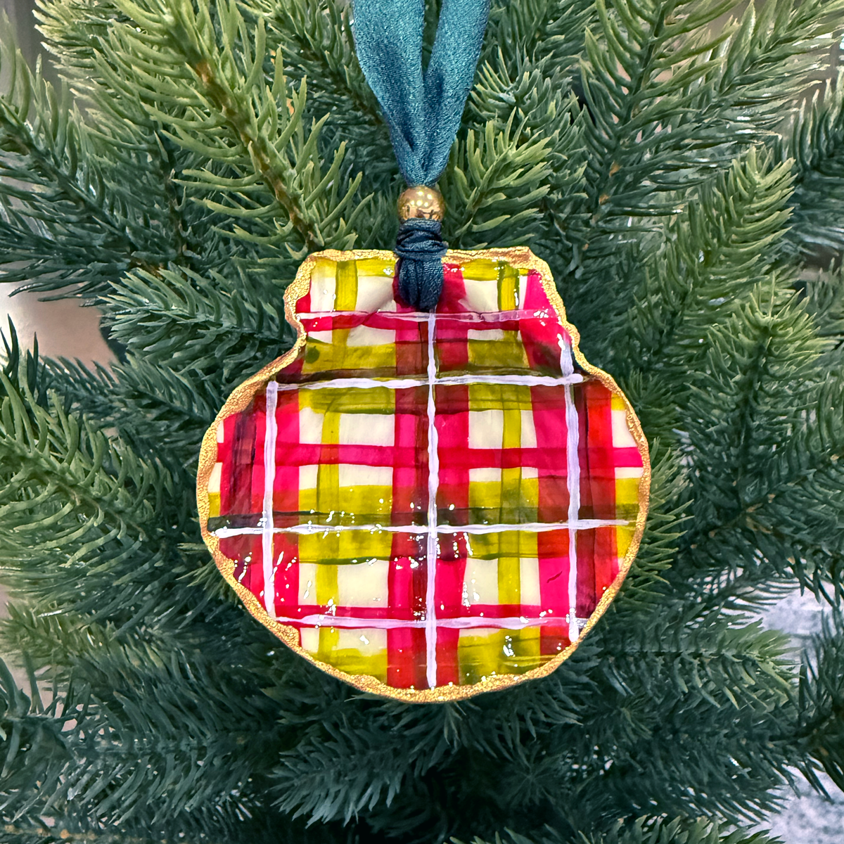 Plaid painted shell ornament hanging on a Christmas tree
